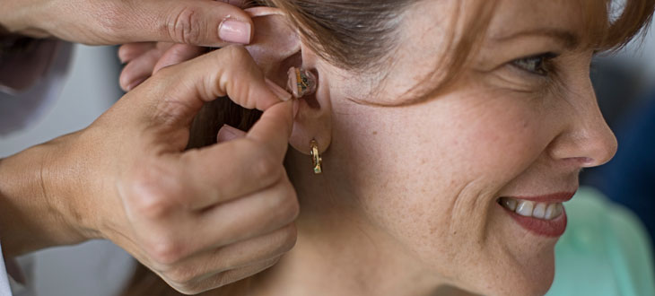 Woman with red hair being fit with an invisible in the canal hearing aid in her right ear
